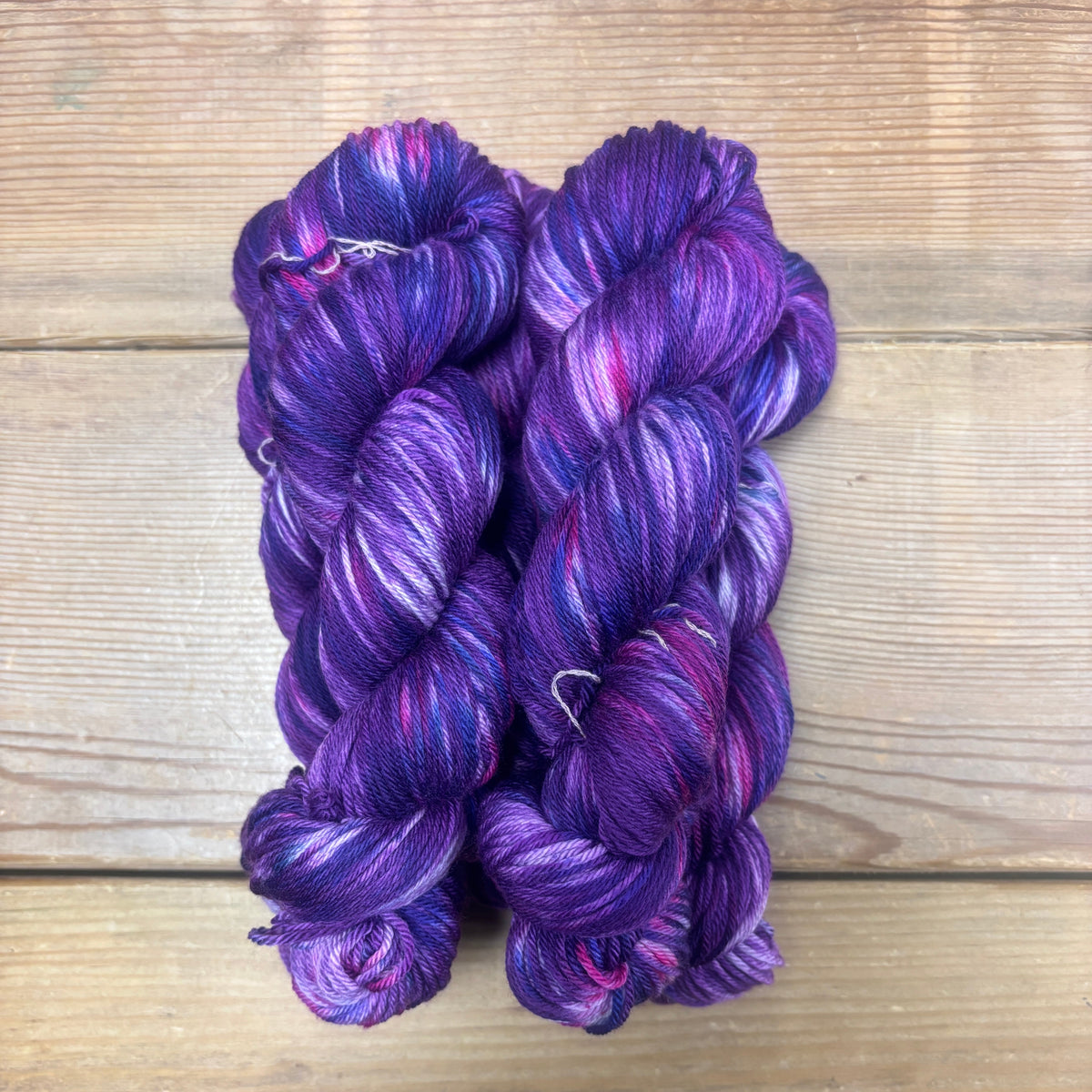 Three skeins of purple yarn on a wooden surface