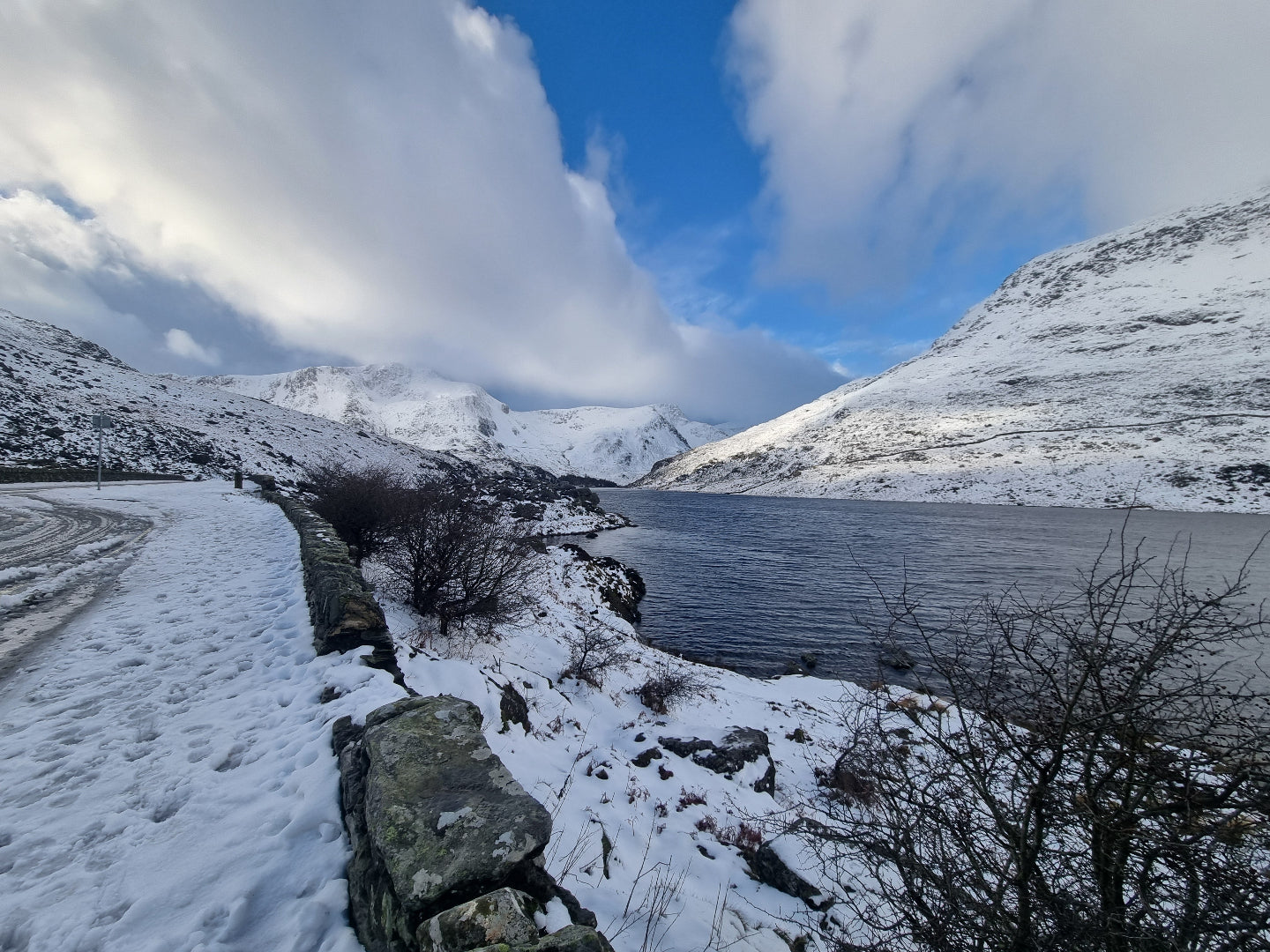 Snowy landscape with a lake and mountains under a blue sky.