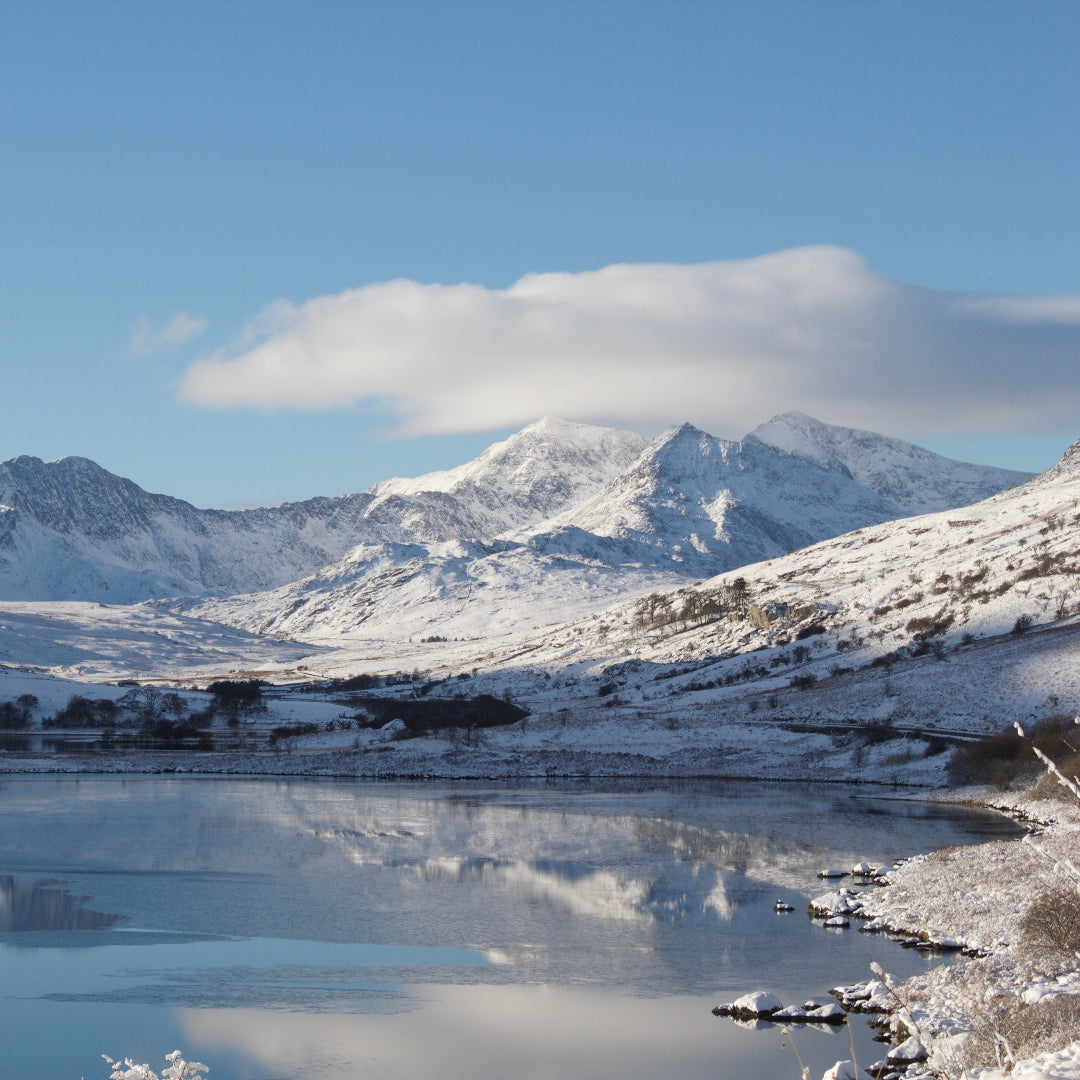 Snow-covered mountains reflected in a lake with a clear blue sky.