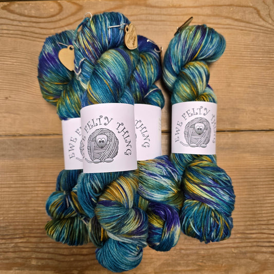 Three skeins of blue and green yarn with labels on a wooden surface